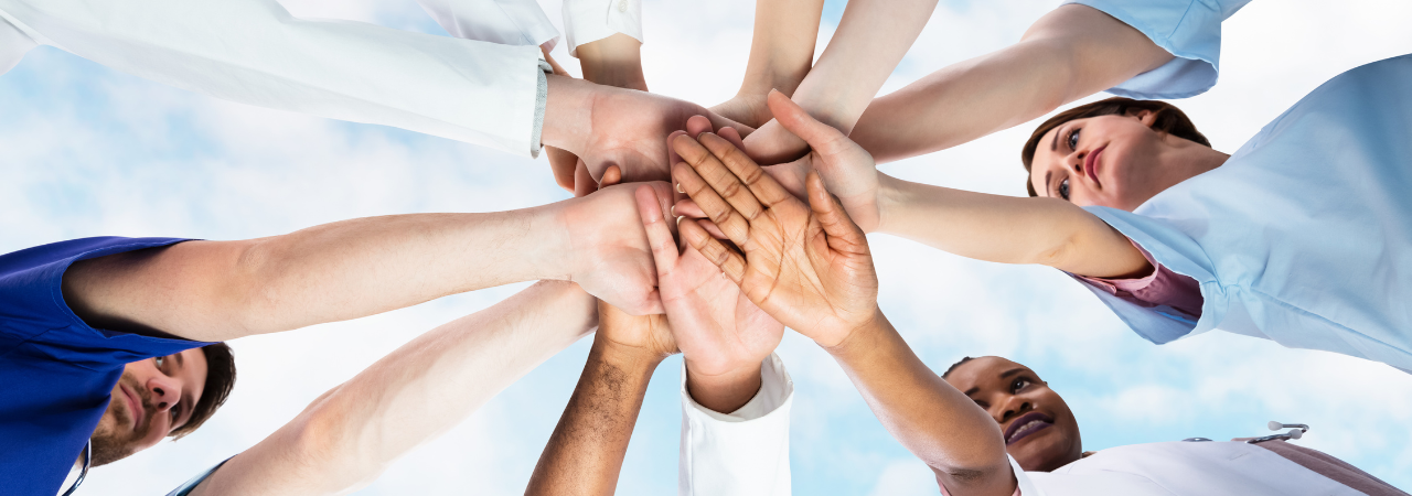 dental staff placing their hands on top of each other in a team huddle